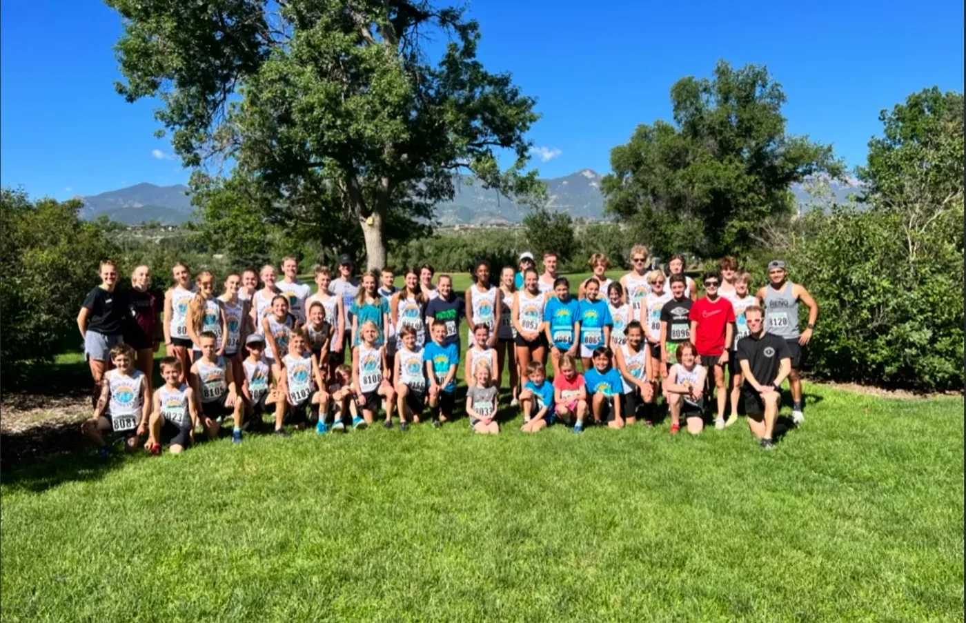A large youth running team gathered outdoors after a race with mountains behind them.